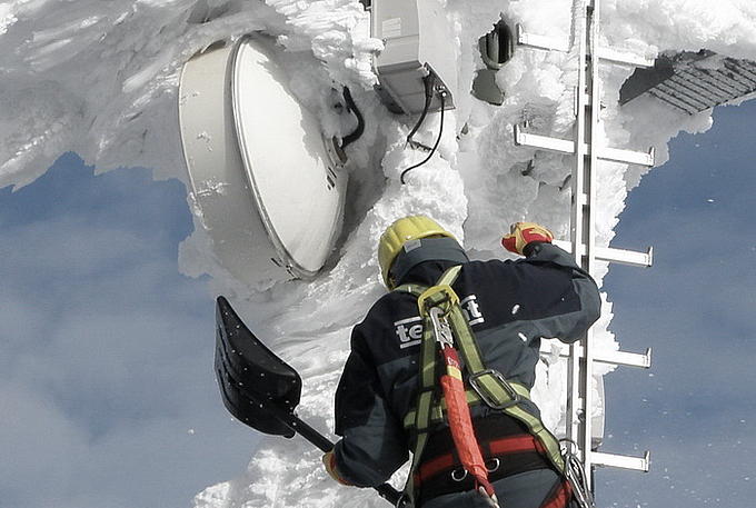 Foto eines Arbeiters, der eine Richtfunkantenne von Schnee befreit.